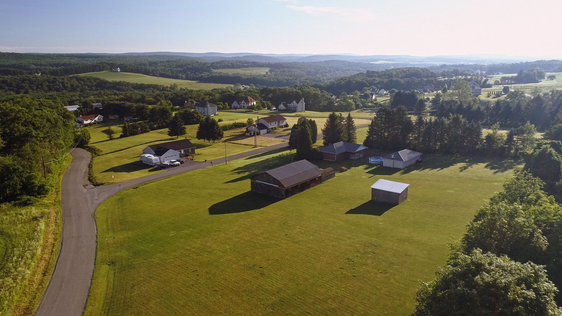 The scenery aerial view of Poconos, Monroe County, Pennsylvania. The sunny summer morning. The panoramic overview over the field and forest to the Kunkletown, then to the small farm near by the road.